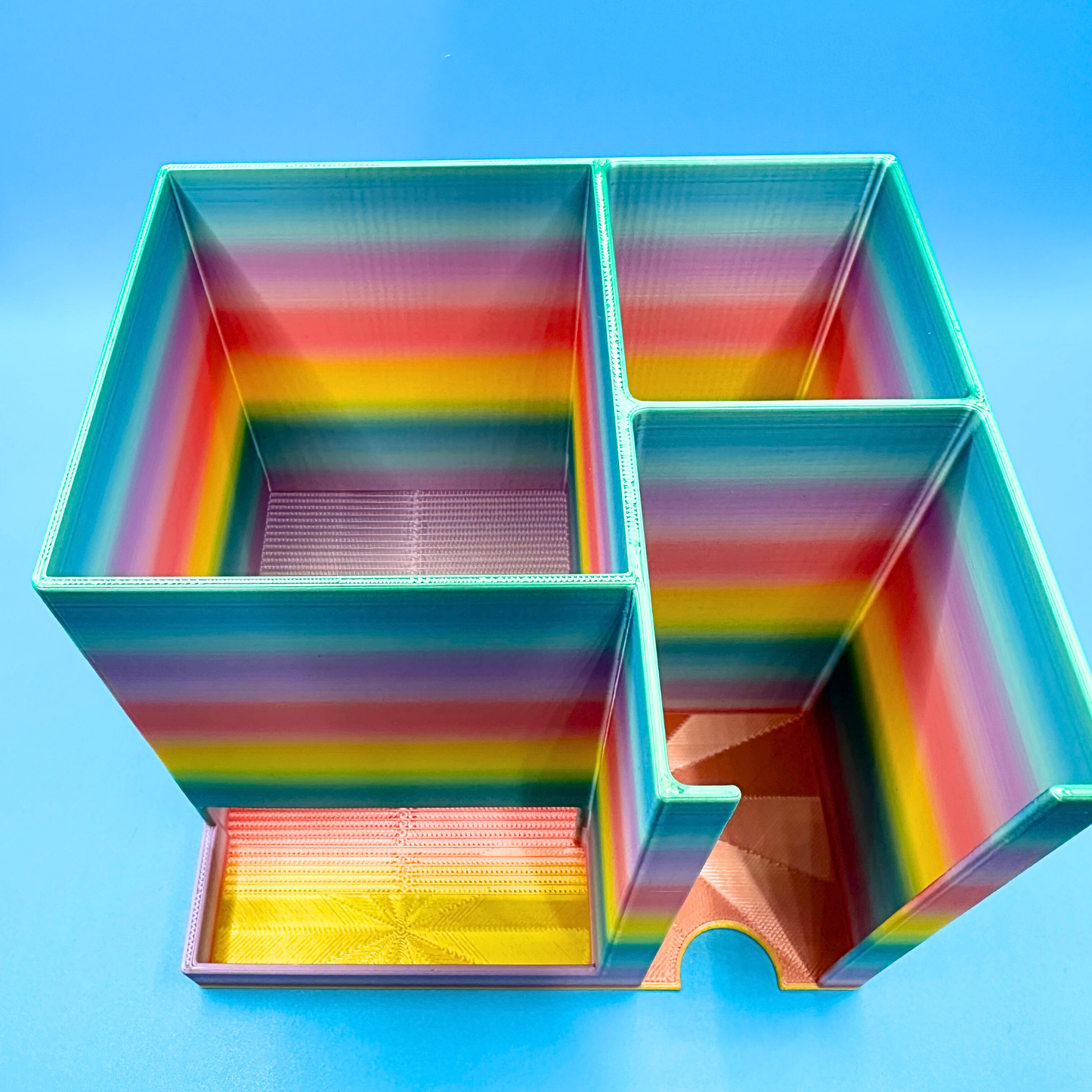 Empty rainbow desktop injection organizer shown from a top-down angle, highlighting the internal compartment layout. The large left compartment is designed to hold a full box of injection pen needles, while the right side features a rear compartment for an injection pen or syringes and a front compartment for alcohol prep pads. Open-top design provides clear visibility and easy access for organized desktop or countertop use.