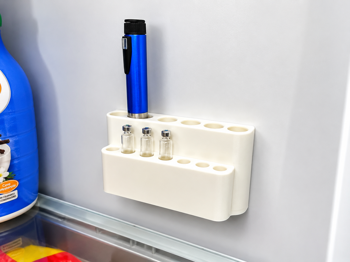 A white plastic magnetic refrigerator organizer holding a blue pen and three small glass vials, mounted on a refrigerator door.