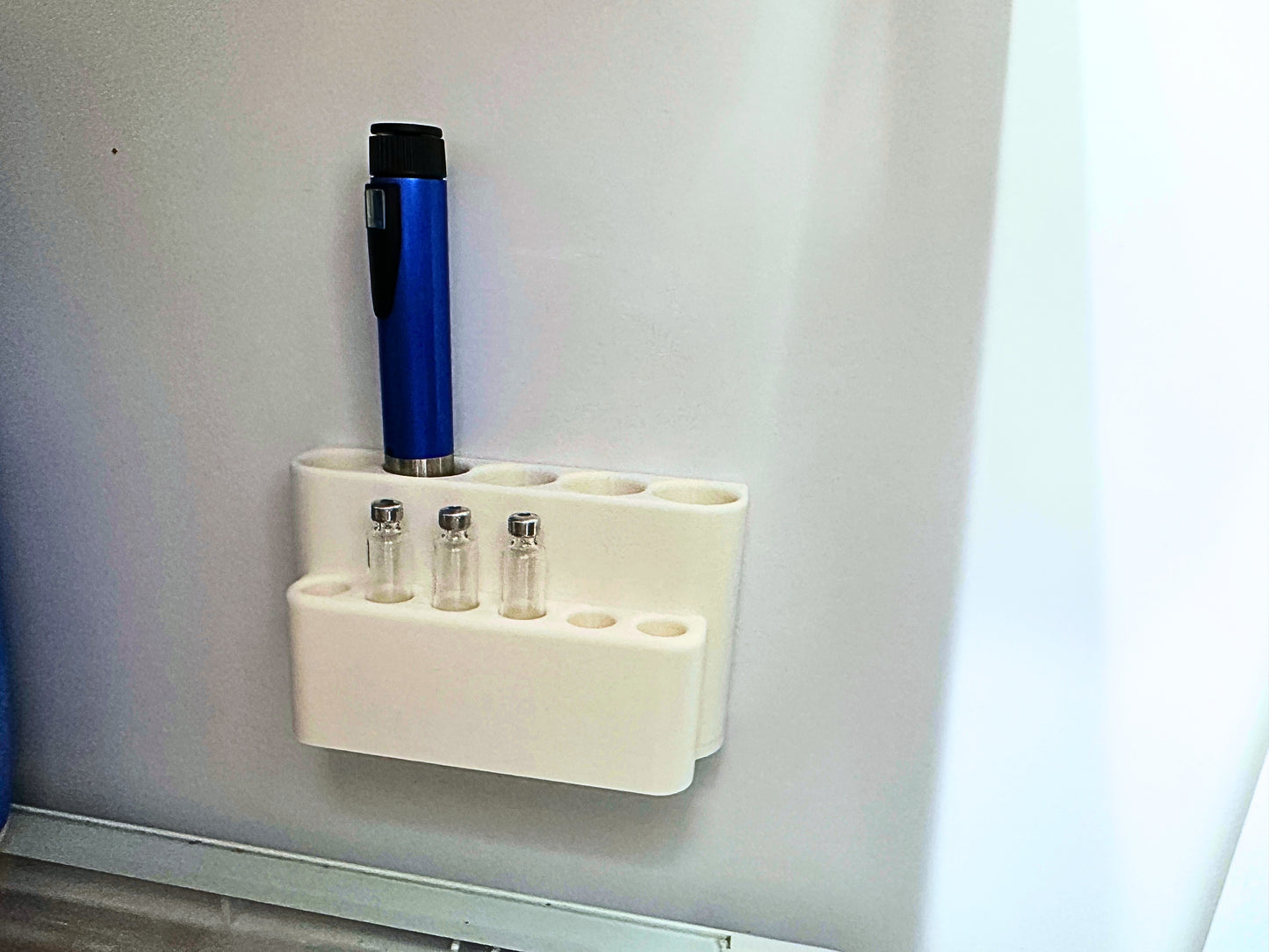 Close-up of wall-mounted pen and cartridge organizer inside fridge with pen slot and 11.5mm cartridge slots visible