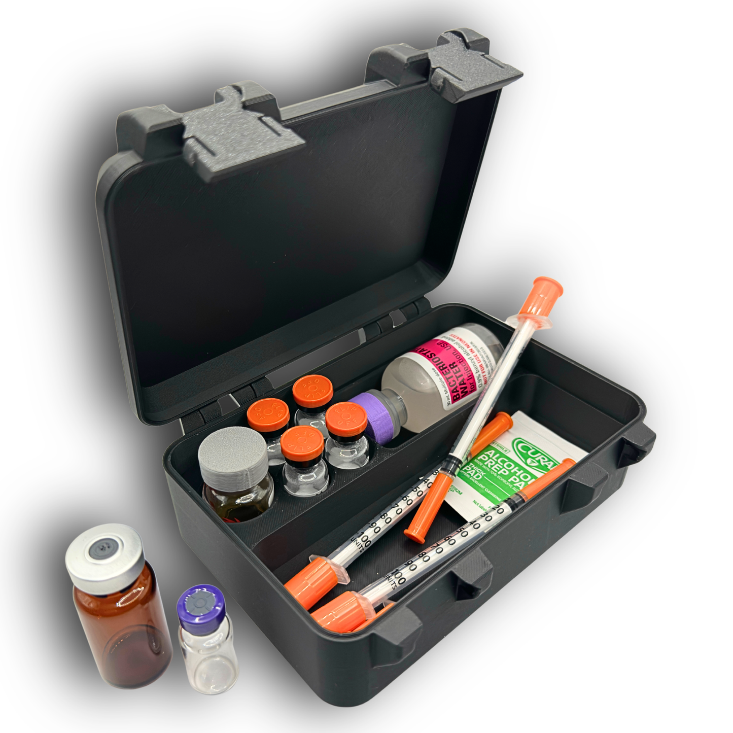 Compact vial and syringe organizer case shown open at an angle with example contents for size reference. Interior includes one slot for a 10ml vial, four slots for 3ml vials, an oversized vial compartment, and a large section for syringes or wipes. Hinged lid with snap lock closure. Case sold empty.
